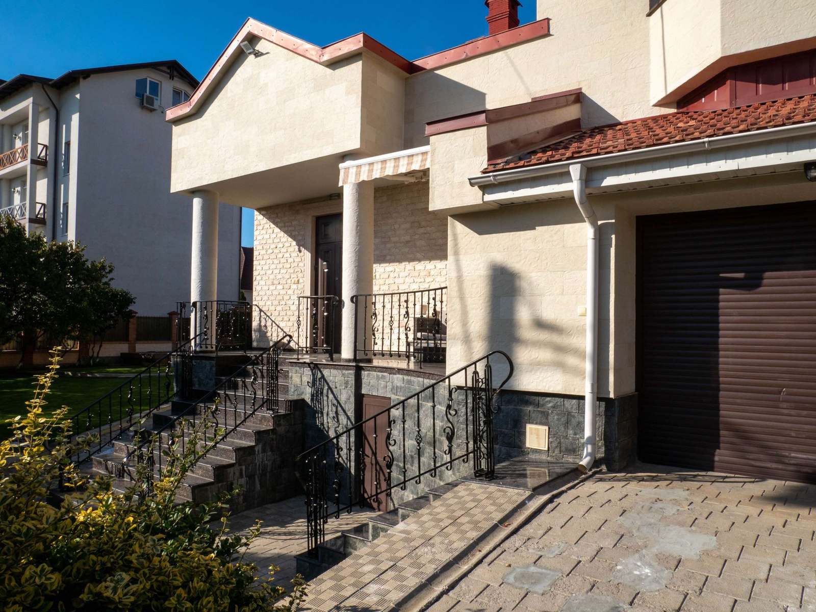 Fațada dinspre stradă cu două uși de garaj maro, trepte și balustrade forjate