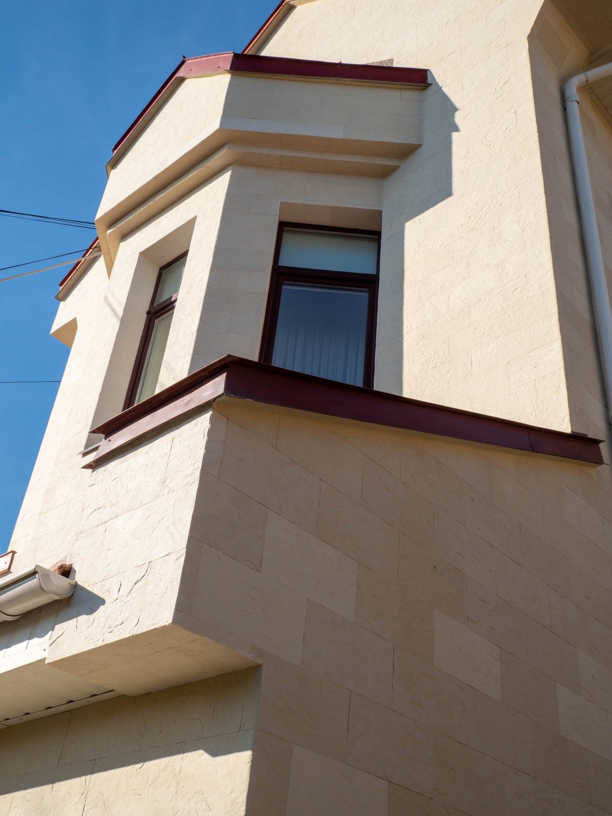 Fronton înalt și bovindou văzute de jos, piatră flexibilă bej și rame de ferestre maro
