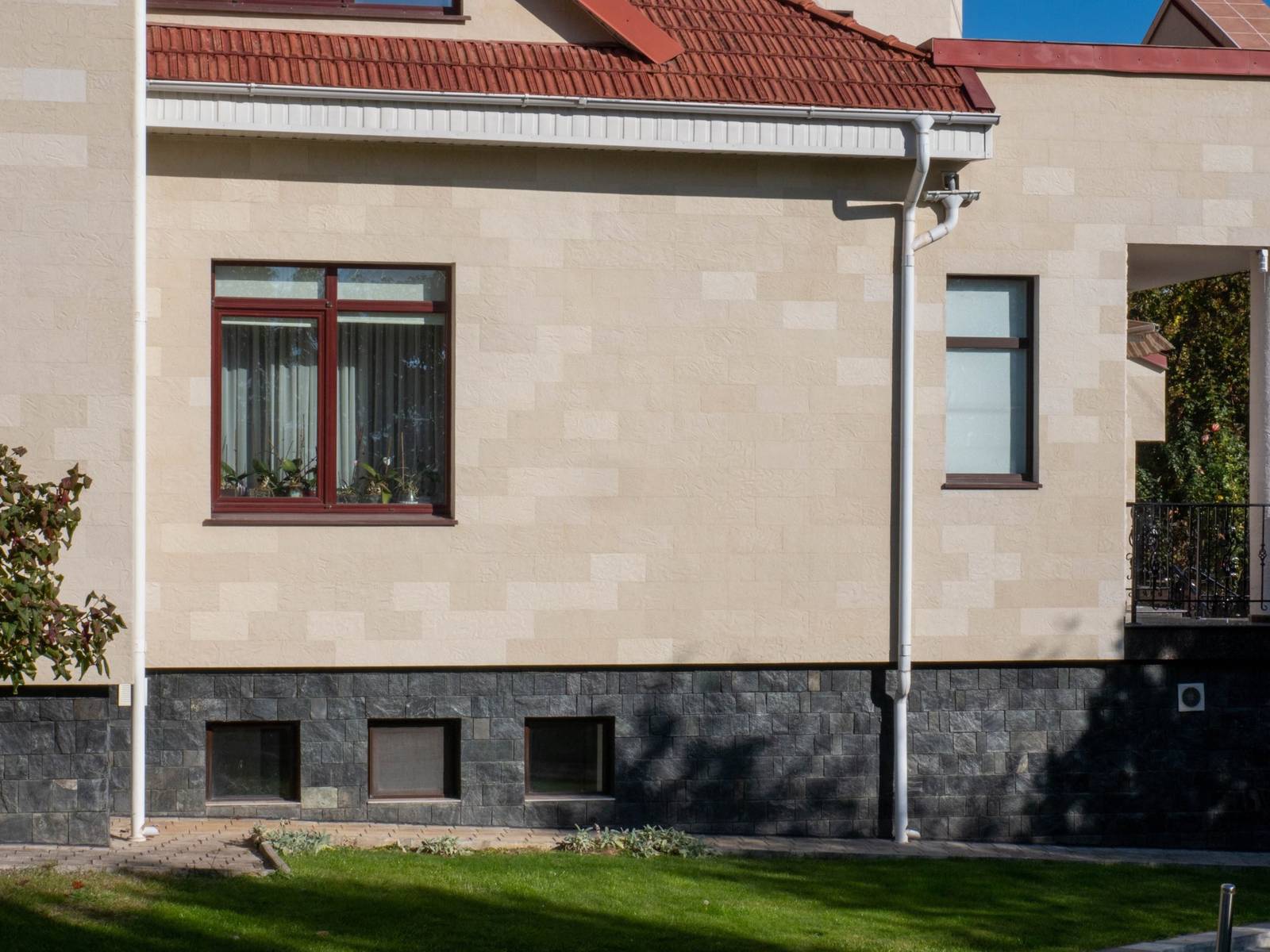Vedere laterală a casei cu ferestre mari și acoperiș roșu, placare din piatră flexibilă bej