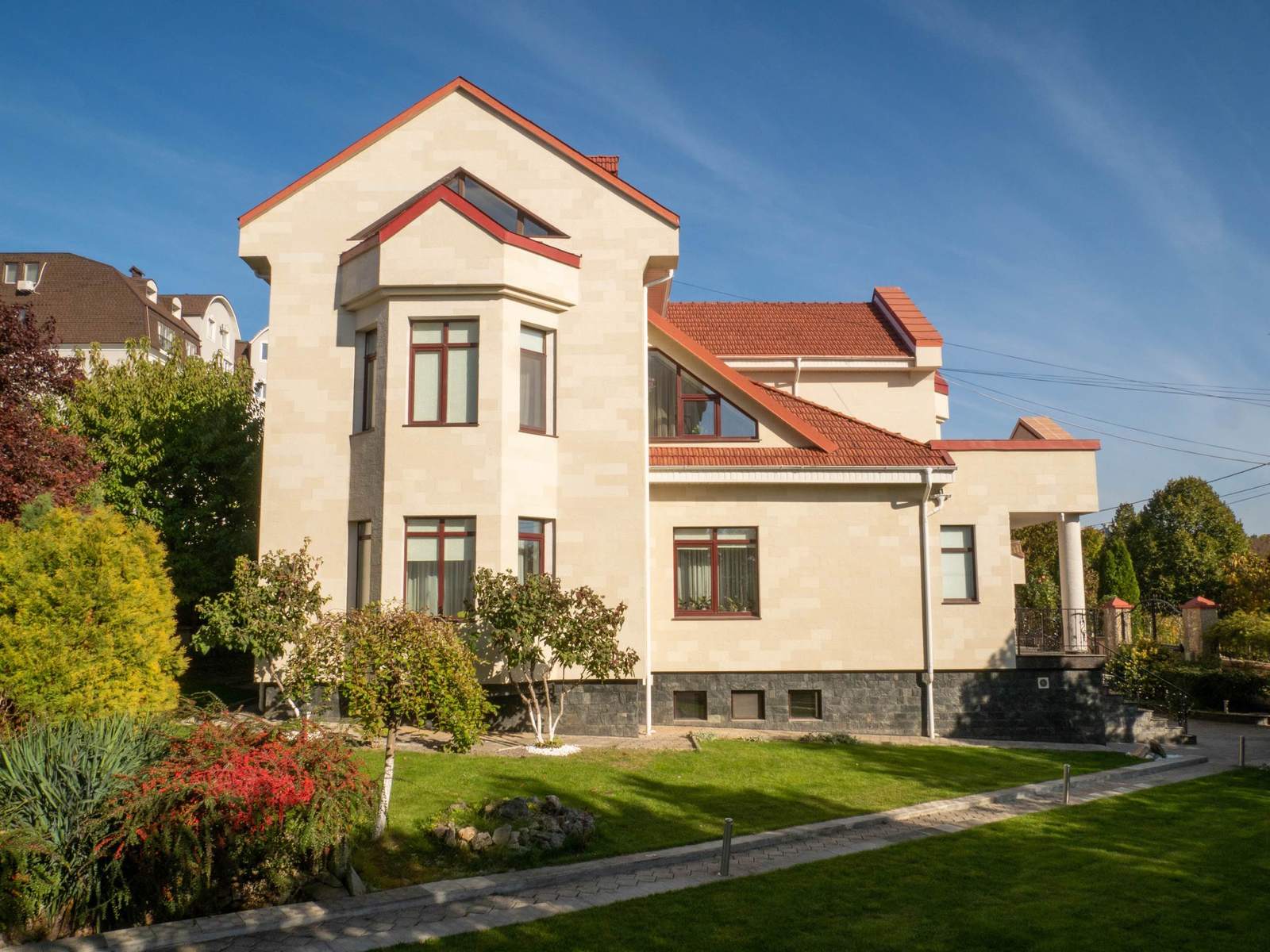 Vedere laterală a casei: frontoane înalte, acoperiș roșu și fațadă din piatră flexibilă Tender Rock, cu gazon